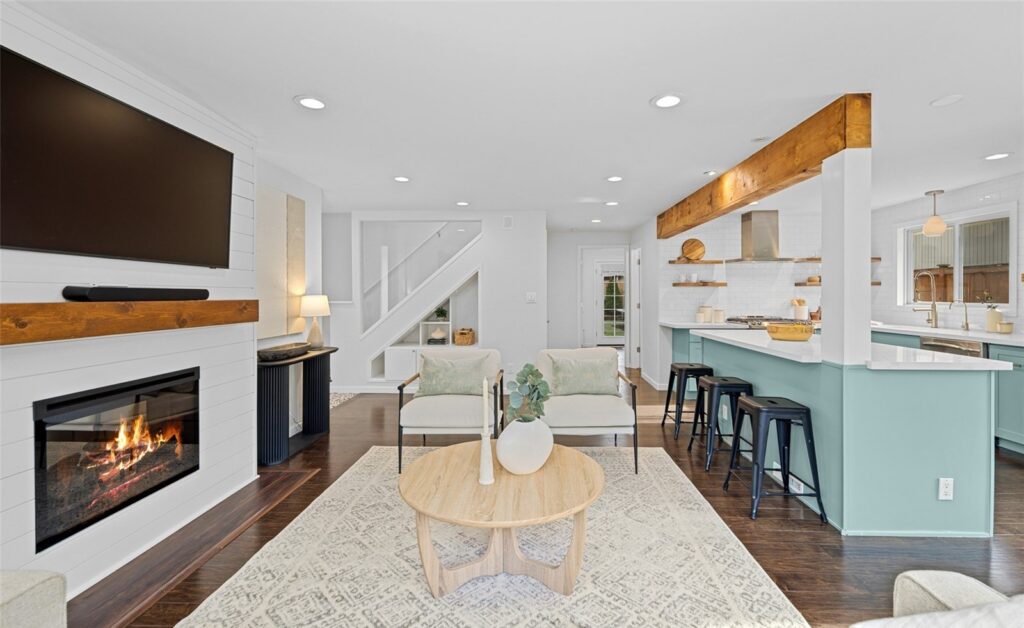 Living area with a fireplace and a reclaimed wood beam, open to the kitchen
