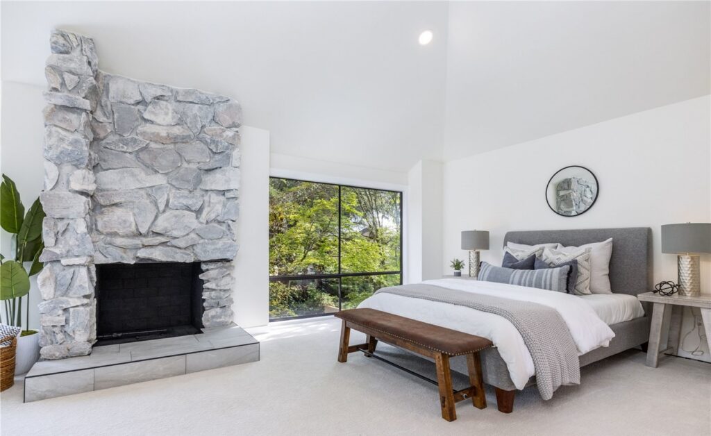 Primary bedroom with an upholstered bed beside a stone fireplace in a staged Redmond townhome