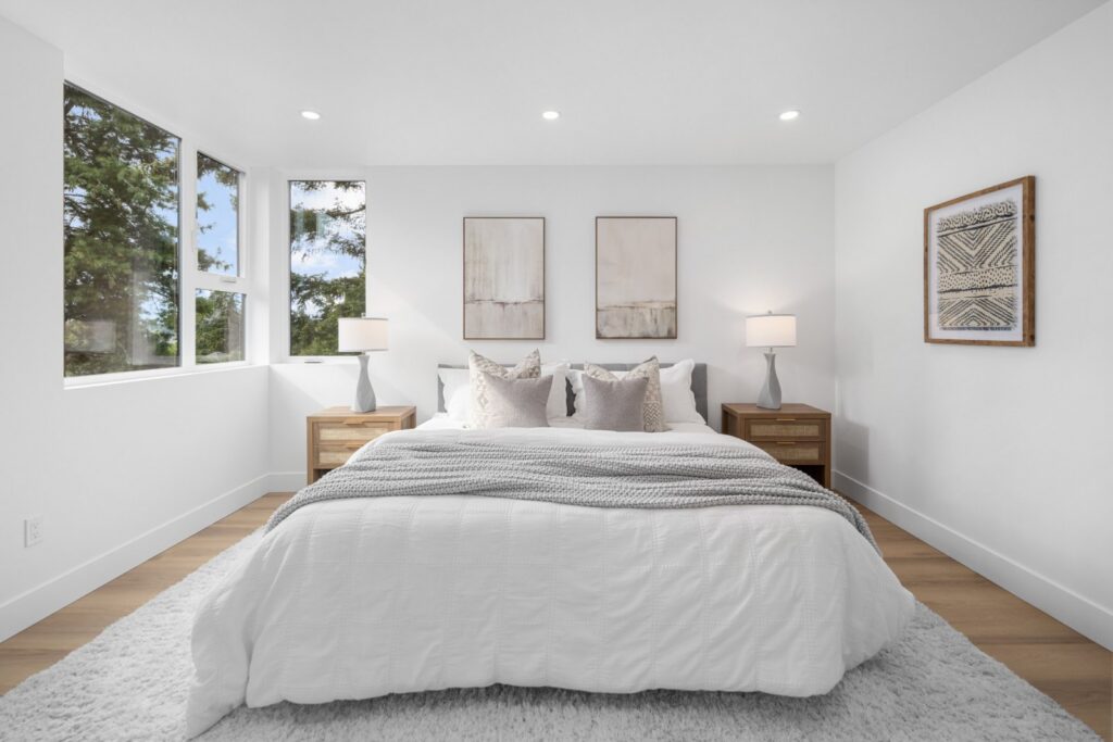 Bedroom with a white upholstered bed, layered pillows and paired art in a Seattle townhouse